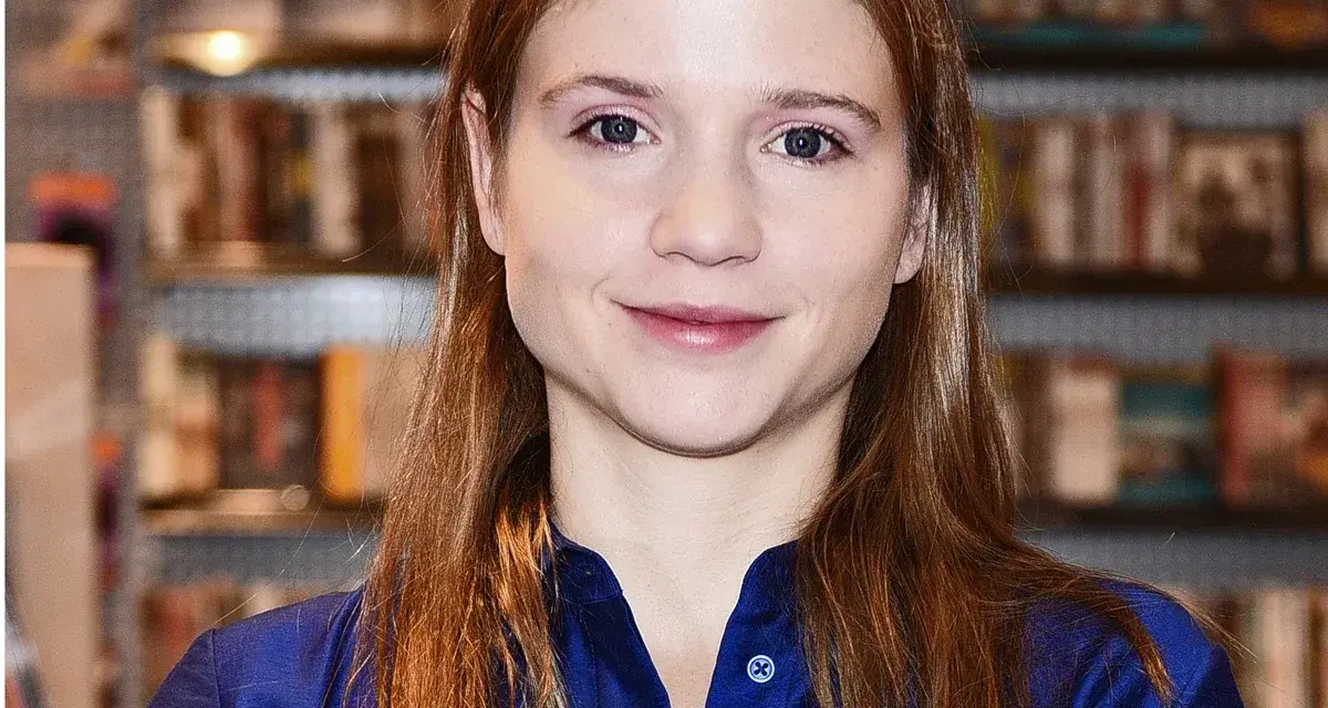 Eliza Rycembel, uśmiechnięta, w niebieskiej bluzce, na tle regałów z książkami. Jej życie prywatne jest tematem zainteresowania.