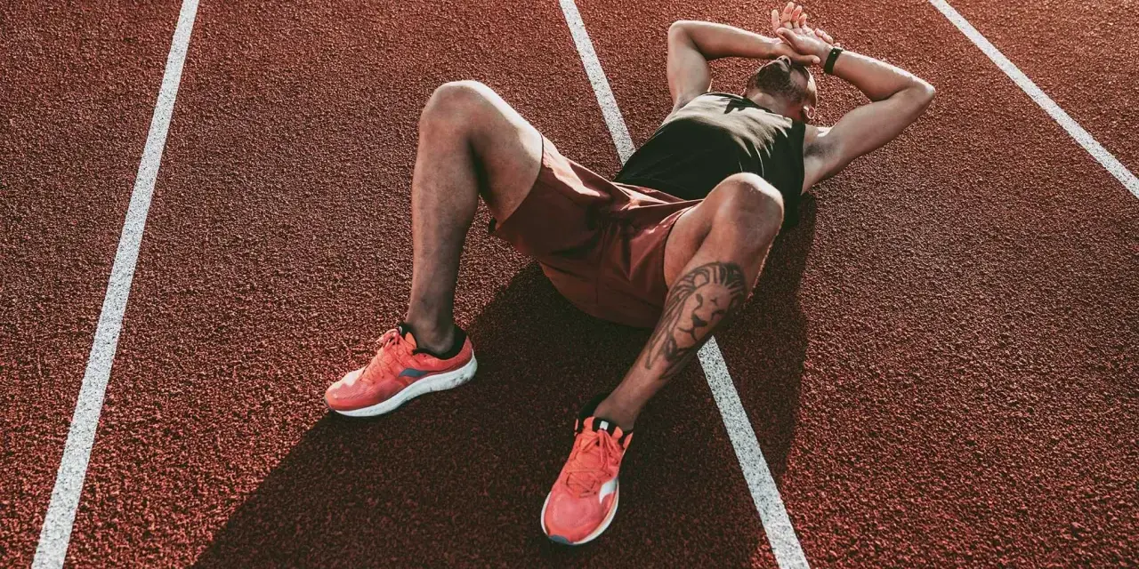 Atleta esausto sdraiato su una pista da corsa, con le mani sulla testa, forse vittima della sindrome da overtraining.