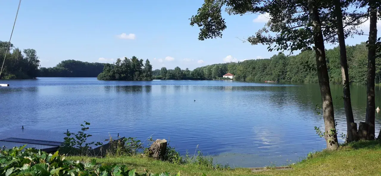 Ein ruhiger Lippstadt See mit bewaldeten Ufern und einem kleinen Haus am Horizont.