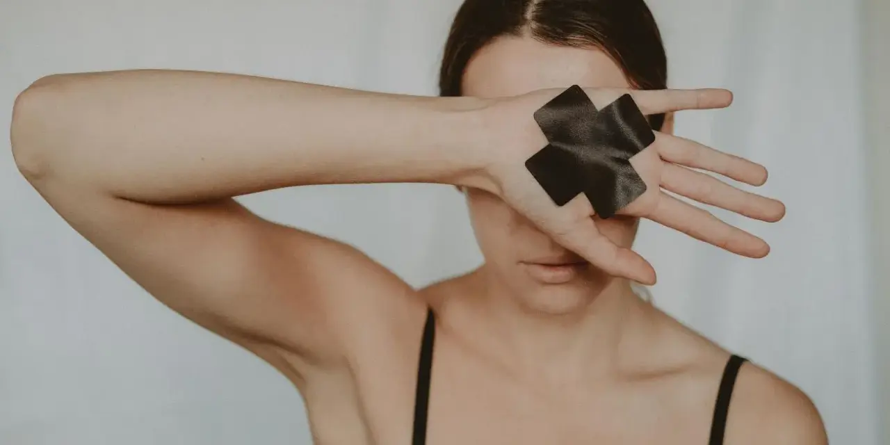 Kobieta zakrywa oczy dłonią z czarną taśmą w kształcie krzyża, symbolizującą trauma seksualna i potrzebę uzdrowienia.