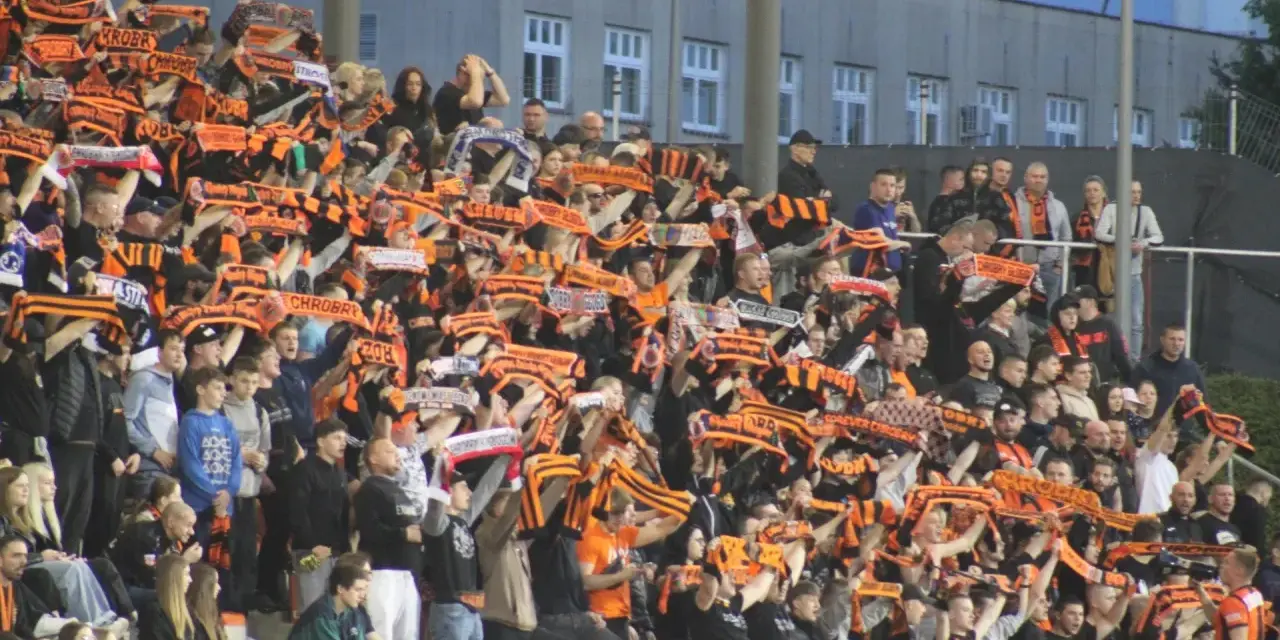Tłum kibiców na stadionie z szalikami w barwach pomarańczowo-czarnych. Widać napisy "Chrobry" i "Chrobry Głogów".