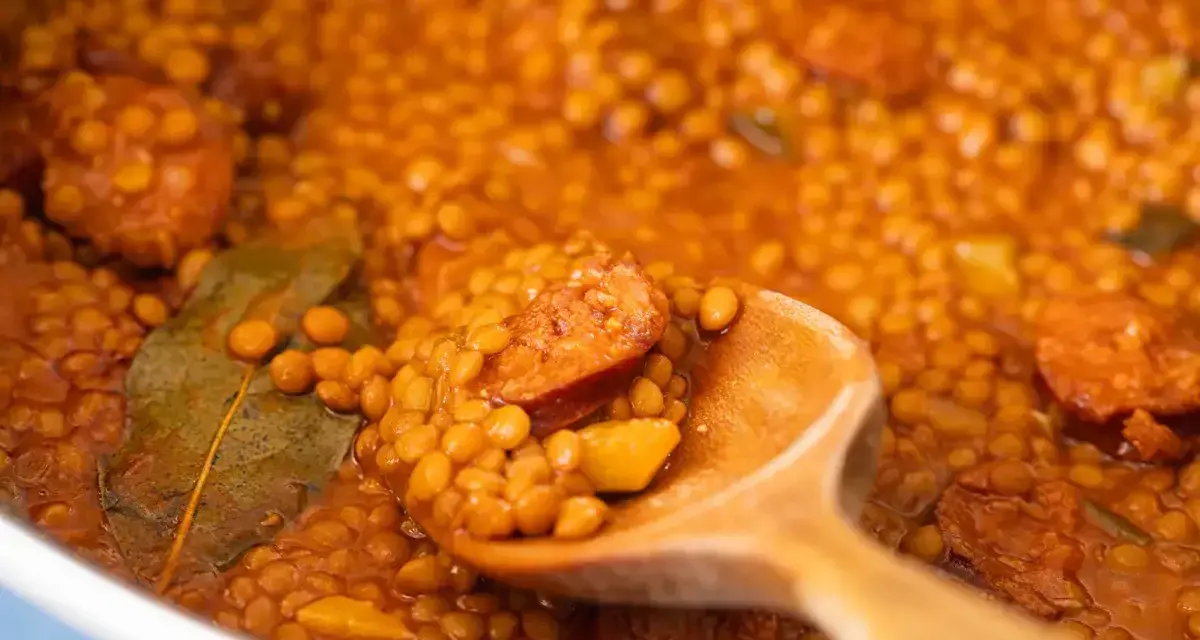 Primer plano de lentejas con chorizo y laurel en una cuchara de madera.