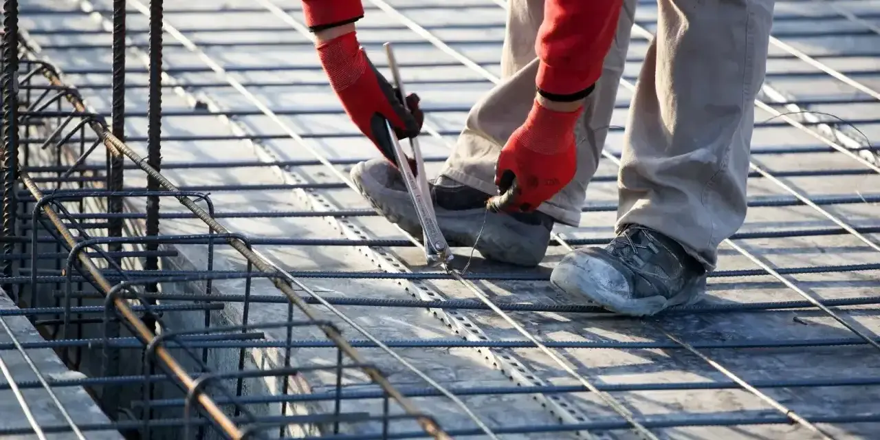 Budowlaniec wiąże zbrojenie. To kluczowy etap budowy, który wpływa na to, ile stali na dom 100m2 będzie potrzebne.