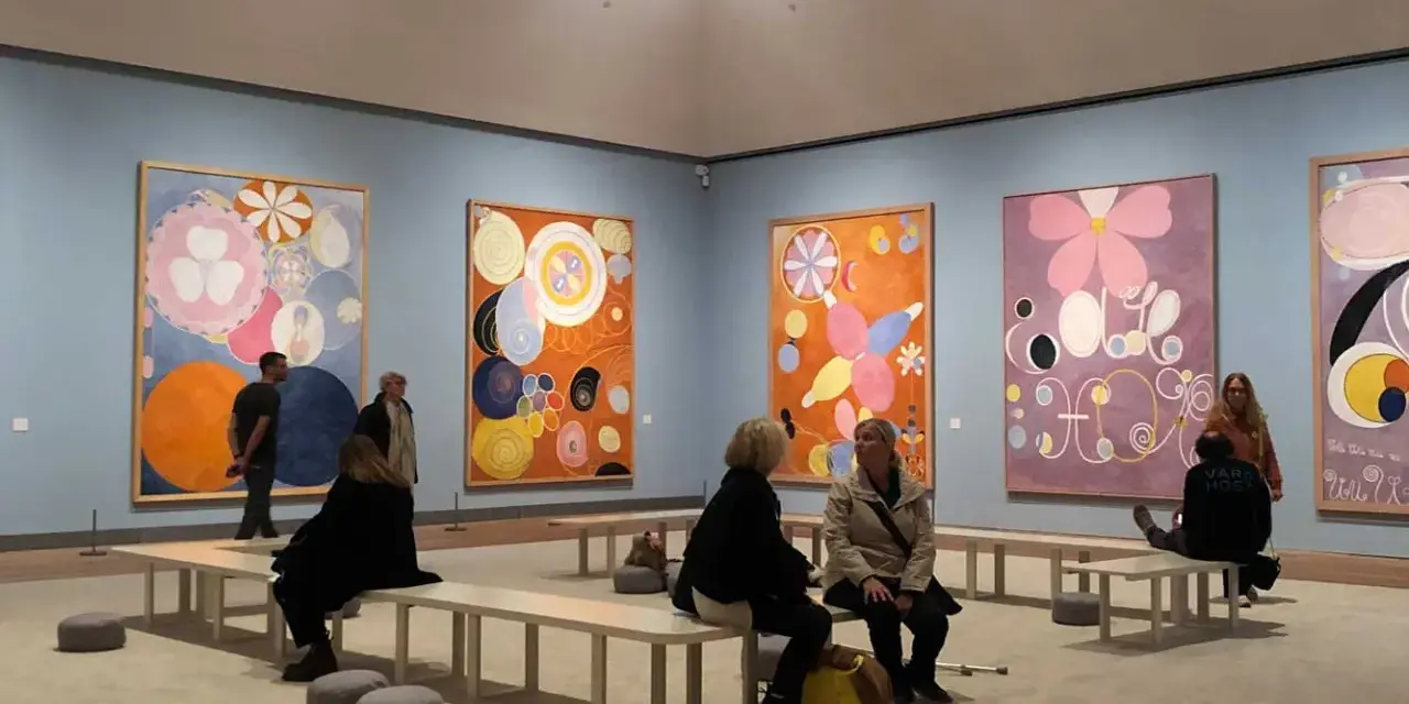 Besökare beundrar Hilma af Klints färgstarka verk i ett galleri. En familj kanske diskuterar konstens mystik.
