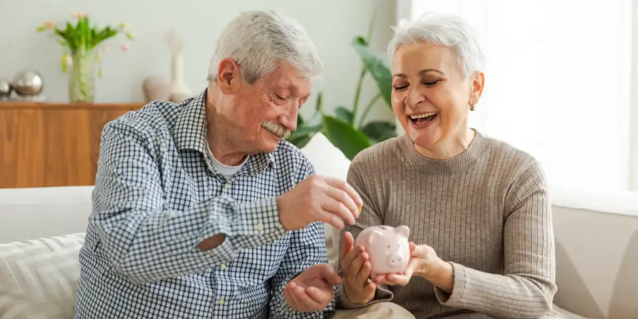 Szczęśliwa para seniorów wrzuca monety do świnki-skarbonki, planując spokojne przejście na emeryturę.