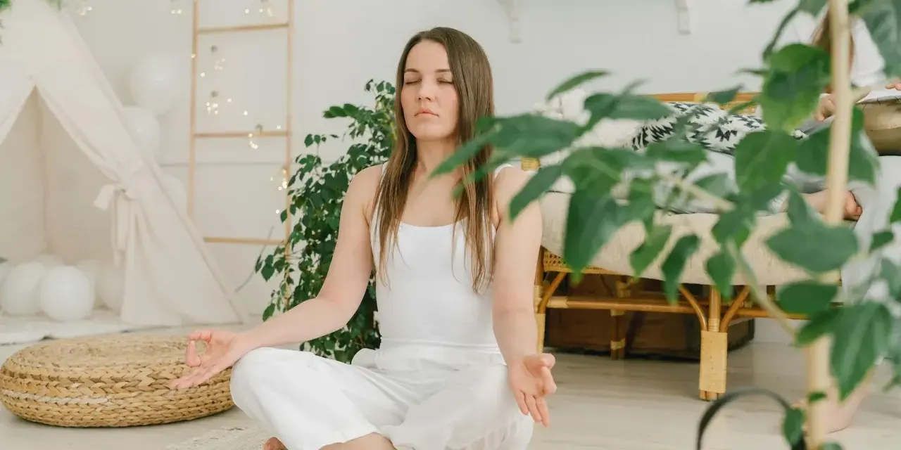 Frau in weißer Kleidung meditiert im Lotussitz. Eine sanfte Metta-Meditation-Anleitung textlich wäre hier passend.
