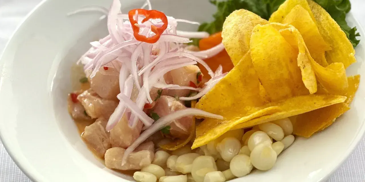 Delicioso ceviche peruano con trozos de pescado fresco, cebolla morada, chile, maíz tierno y chips de plátano.