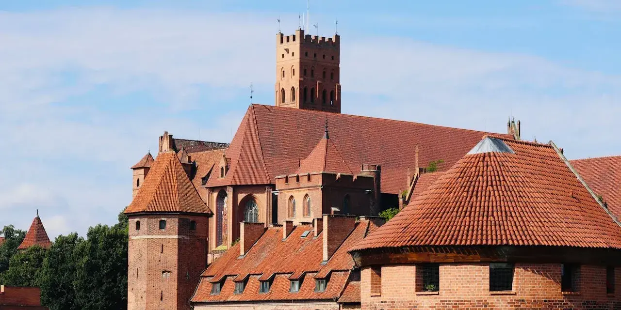 Zamek w Malborku, wpisany na listę **UNESCO Polska**, to imponująca twierdza z czerwonej cegły z charakterystycznymi wieżami i dachami.