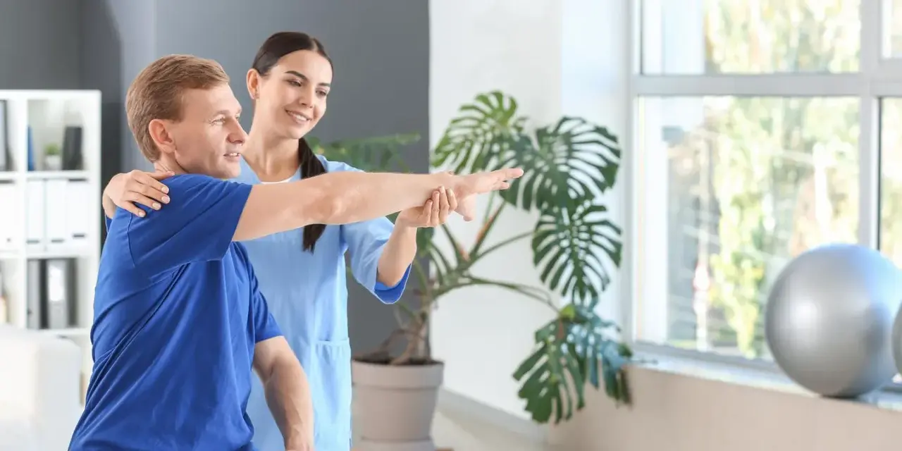 Ein Physiotherapeut unterstützt einen Patienten bei der Armbewegung.