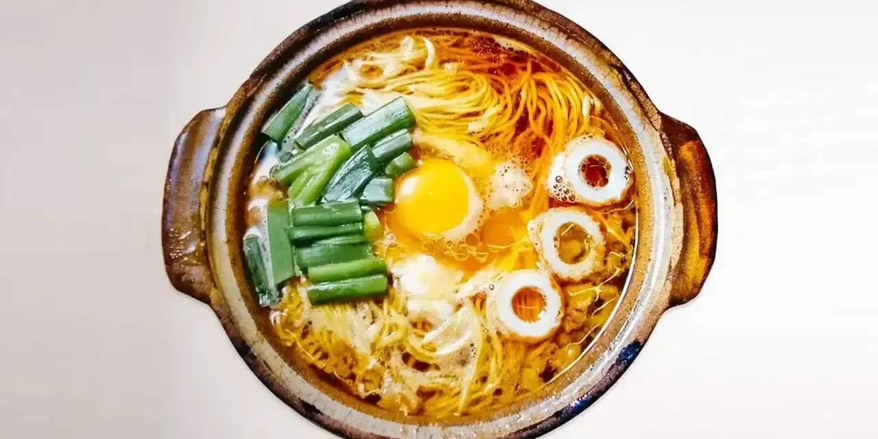 Gorący garnek z aromatycznym bulionem, żółtkiem jajka, zielonym szczypiorkiem i krążkami rybnymi. Czy to ramen czy udon?
