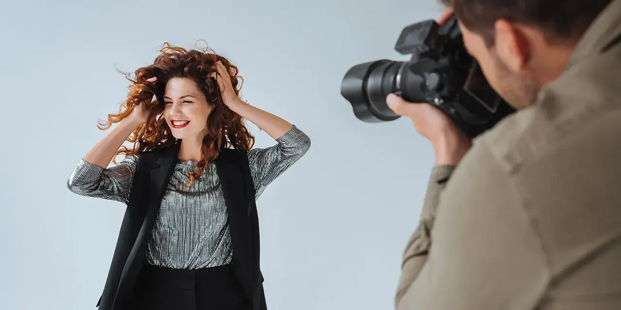 Modelka z burzą rudych włosów pozuje do zdjęcia. Fotograf robi jej zdjęcie. To sesja TFP, co to znaczy?