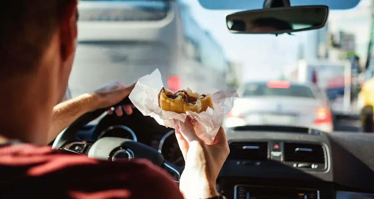 Uomo al volante mangia un panino in un ingorgo. Si può mangiare mentre si guida, ma attenzione alla sicurezza!