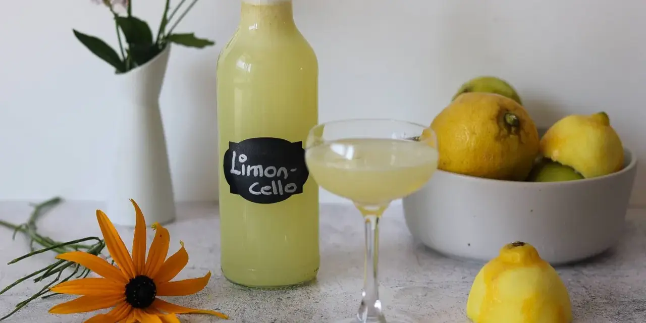 Erfrischendes Limoncello Eis, serviert in einem Glas, neben einer Flasche und frischen Zitronen. Ein gelber Sonnenhut blüht daneben.