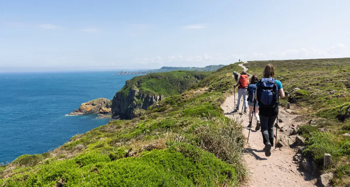Randonneurs sur le sentier côtier GR34, profitant de la vue sur la mer et les falaises. La distance semble longue, mais le paysage est magnifique.