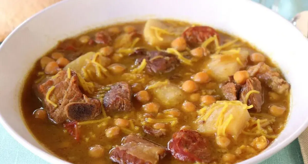 Un reconfortante rancho canario en un cuenco blanco, con garbanzos, trozos de carne, patatas y fideos finos.