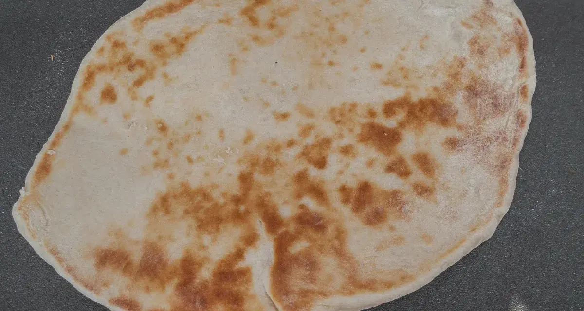Un naan au fromage, peut-être avec un peu de La Vache qui rit, doré et moelleux, prêt à être dégusté.
