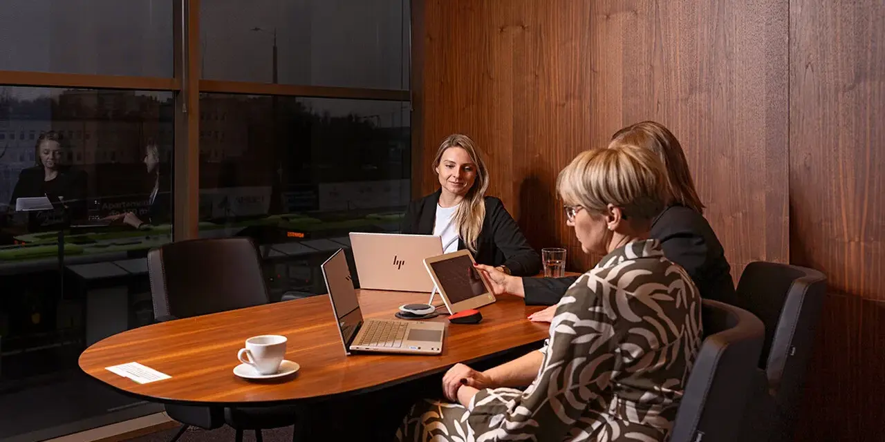 Trzy kobiety omawiają strategię w nowoczesnym biurze. Dyskretne spotkanie, które może dotyczyć usług private banking.