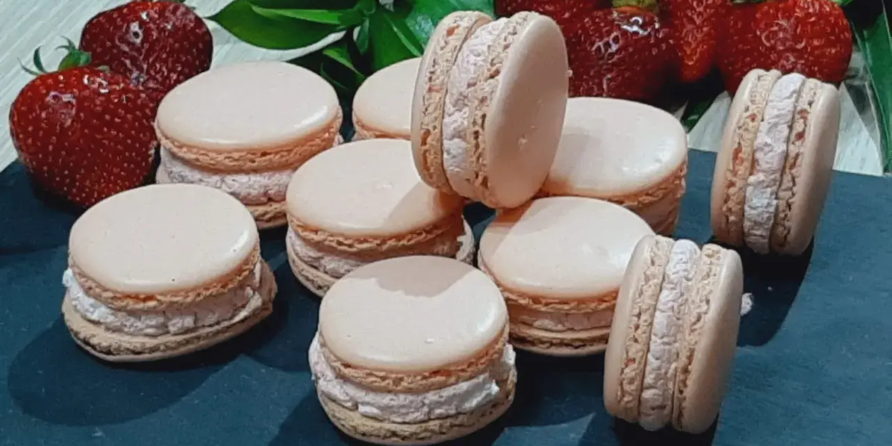 Delikatne makaroniki na mące migdałowej lub kokosowej, z kremowym nadzieniem i świeżymi truskawkami w tle.