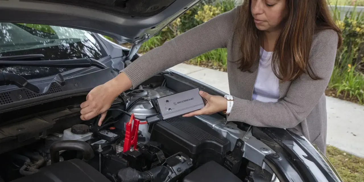 Woman connects a jump starter to a car battery. She's learning how to reset my jump starter.