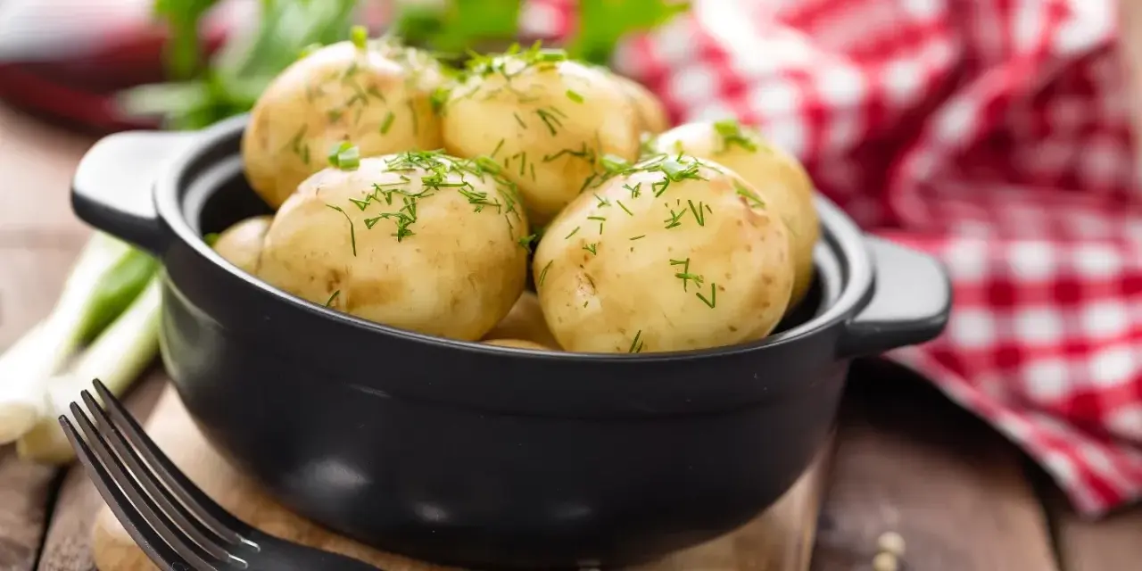 Gotujesz ziemniaki na ból ucha? Te młode ziemniaczki, posypane koperkiem, wyglądają apetycznie. Obok widelec i czerwono-biała serwetka.