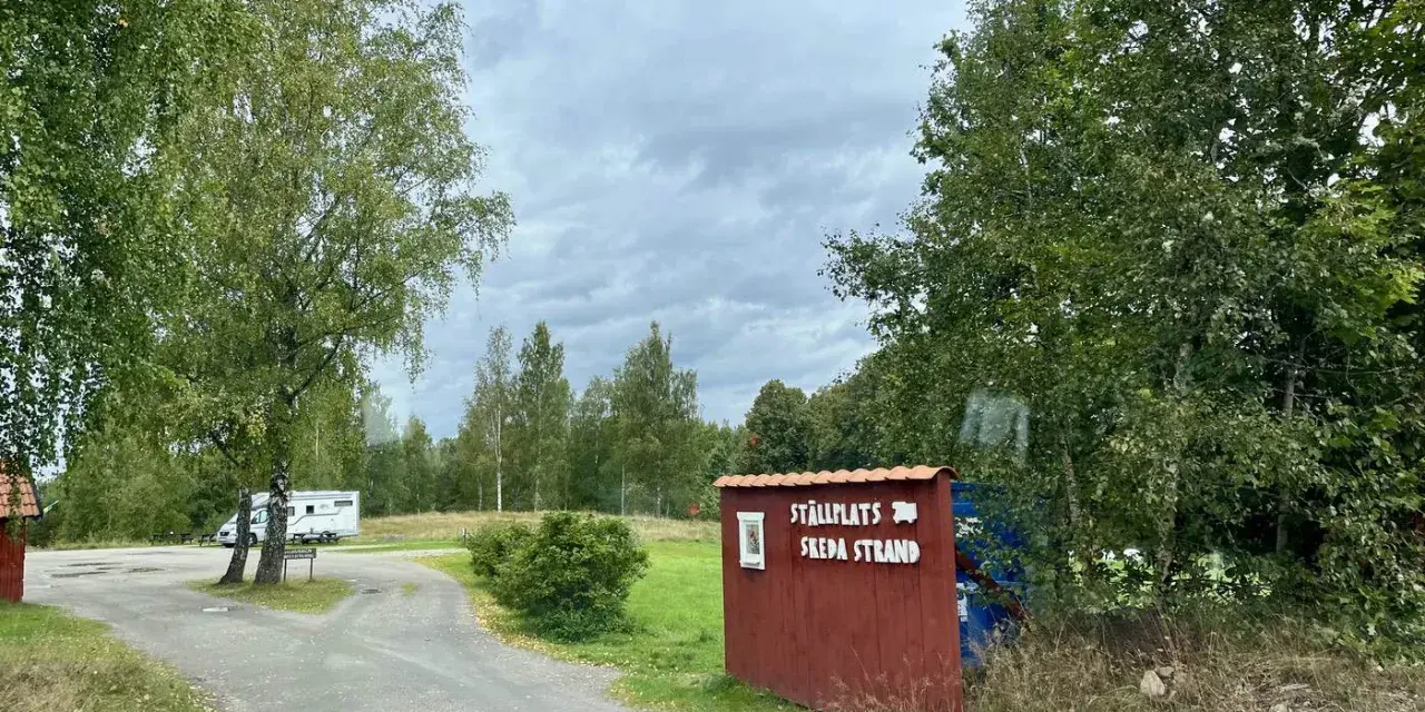 Välkommen till ställplatsen vid Skeda strand. En husbil står parkerad bland träden.