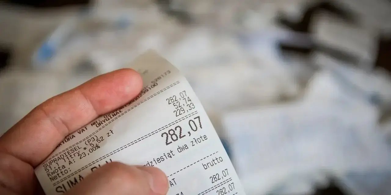Dłoń trzyma paragon z widoczną kwotą 282,07 zł.