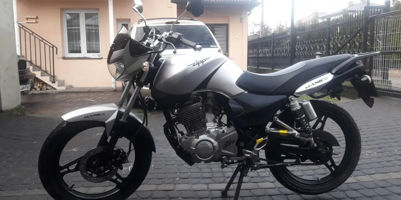 Srebrny Zipp Manic 125 na brukowanym podwórku, gotowy do jazdy.