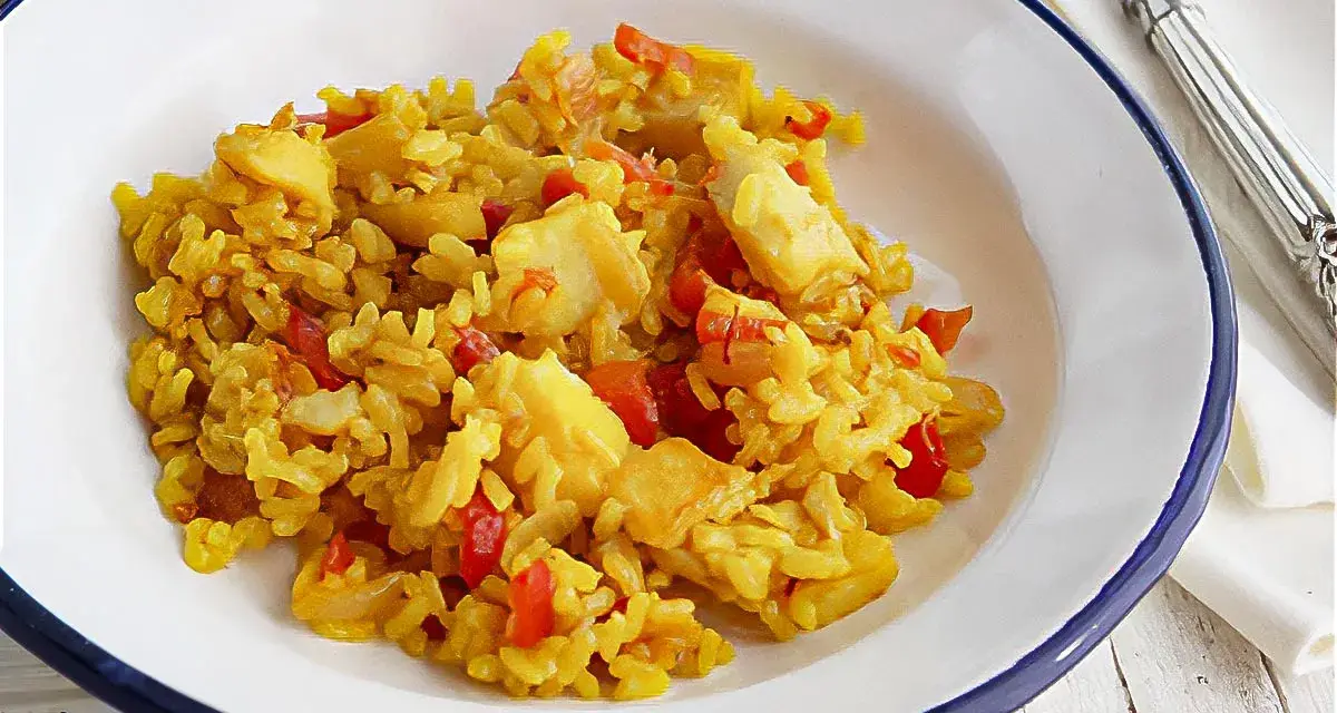 Arroz amarillo con trozos de bacalao y pimientos rojos en un plato blanco.