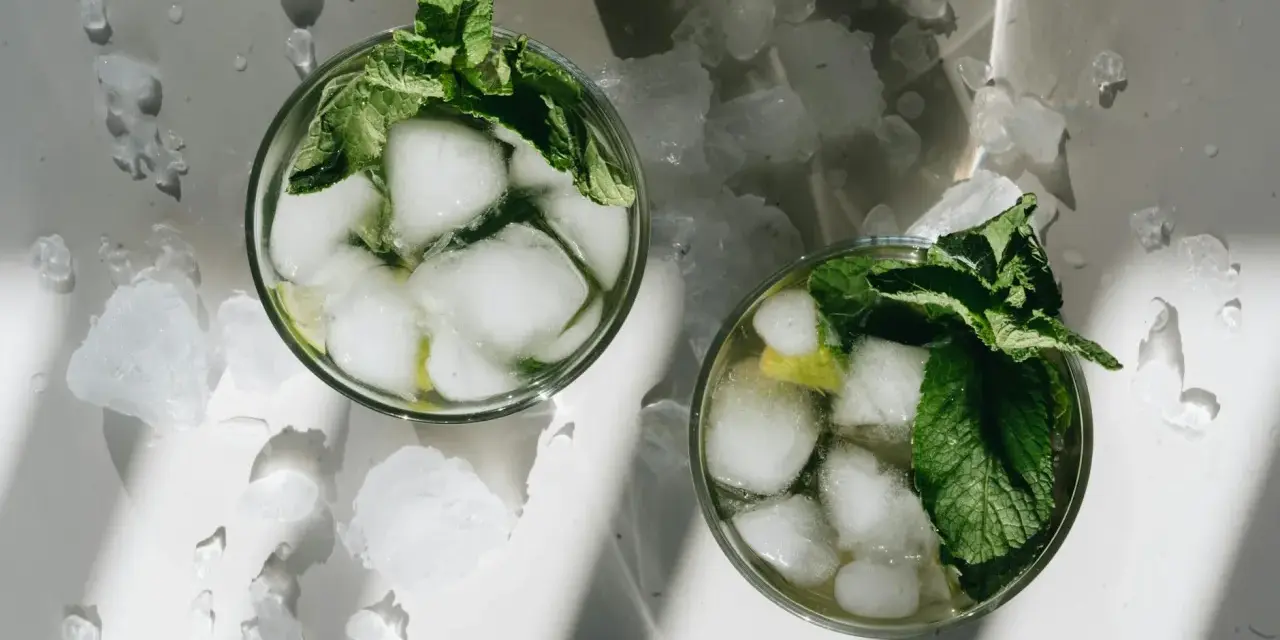 Dwa orzeźwiające mojito z lodem i miętą, otoczone pokruszonym lodem, w letnim słońcu.