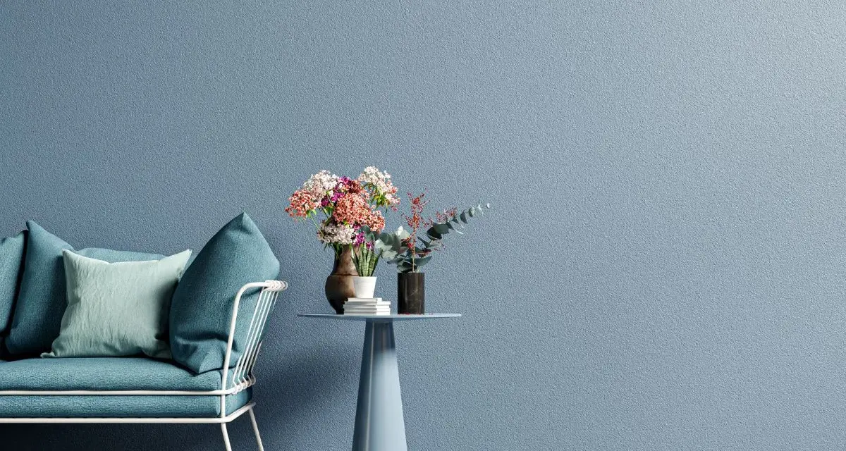 Divano blu e tavolino con fiori su muro azzurro, ispirazione per tecniche di pittura pareti moderne.
