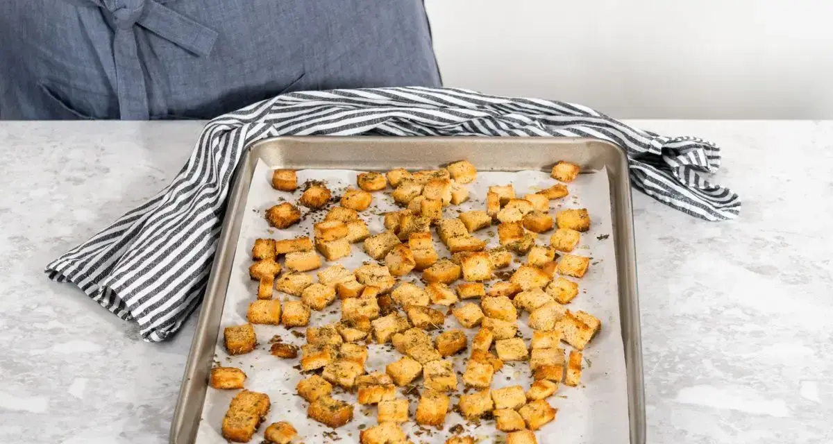 Una teglia piena di crostini di pane dorati e croccanti, conditi con erbe aromatiche. Perfetti per insalate o zuppe.