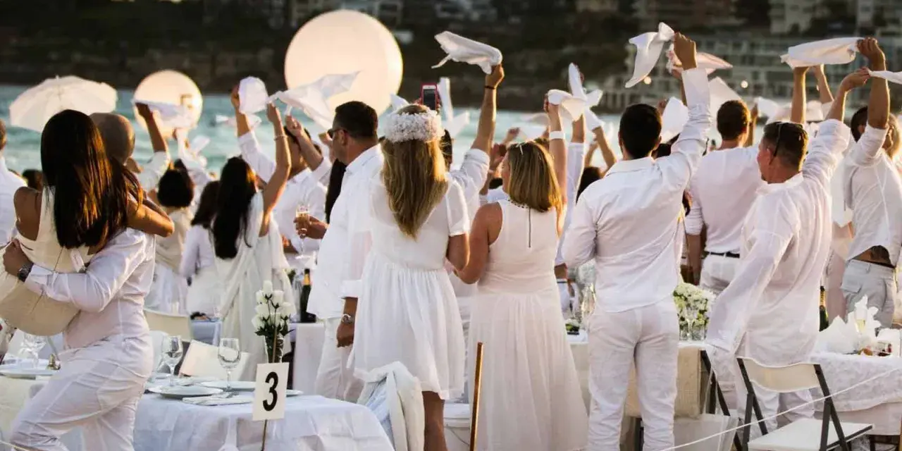 Festa in bianco: tutti vestiti di bianco per un evento elegante sulla spiaggia. Un'atmosfera magica con palloncini luminosi e tavoli apparecchiati.