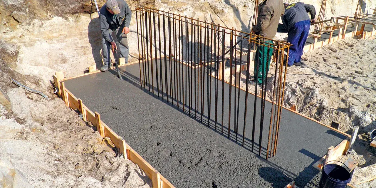 Budowa fundamentów: pracownicy wylewają beton, przygotowując zbrojenie pod przyszły żelbeton.