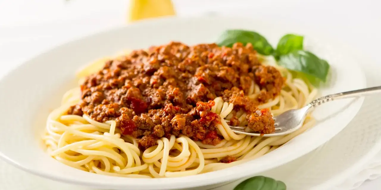 Ein Teller Spaghetti mit einer reichhaltigen, traditionell zubereiteten Bolognese-Sauce, garniert mit frischem Basilikum.