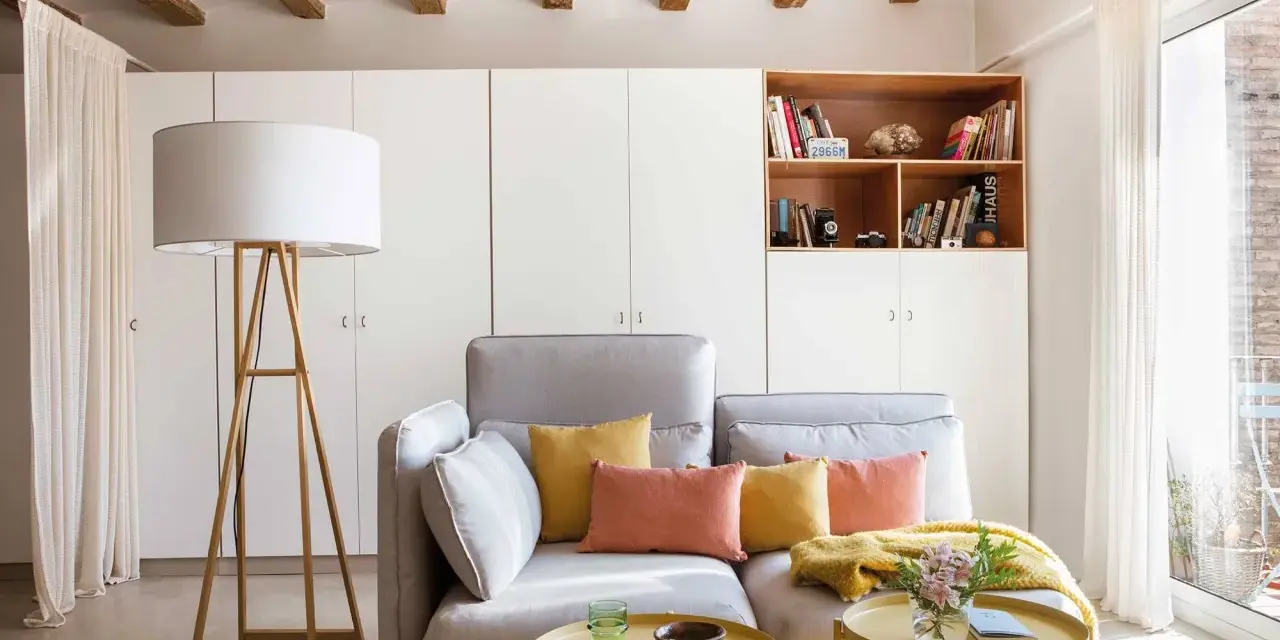 Sofá gris con cojines coloridos, mesa auxiliar amarilla y lámpara de pie. Ideas para decorar piso alquiler low cost con estilo y calidez.