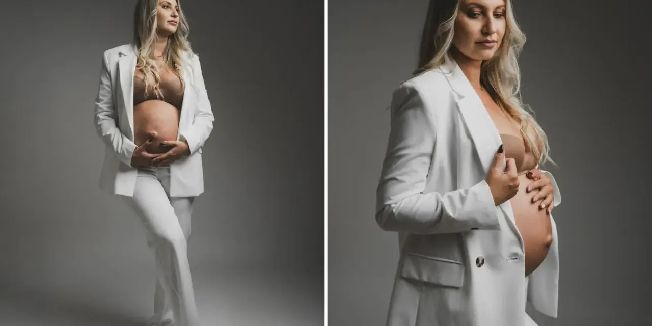 Elegancka kobieta w białym garniturze podczas sesji ciążowej, czule trzymająca się za brzuch.