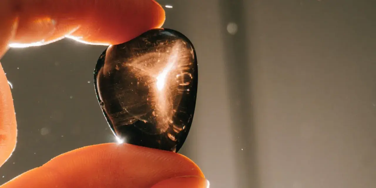 Dedos sostienen una piedra oscura con destellos dorados. ¿Qué pasa si se rompe una piedra energética? Quizás solo se dispersa su luz.
