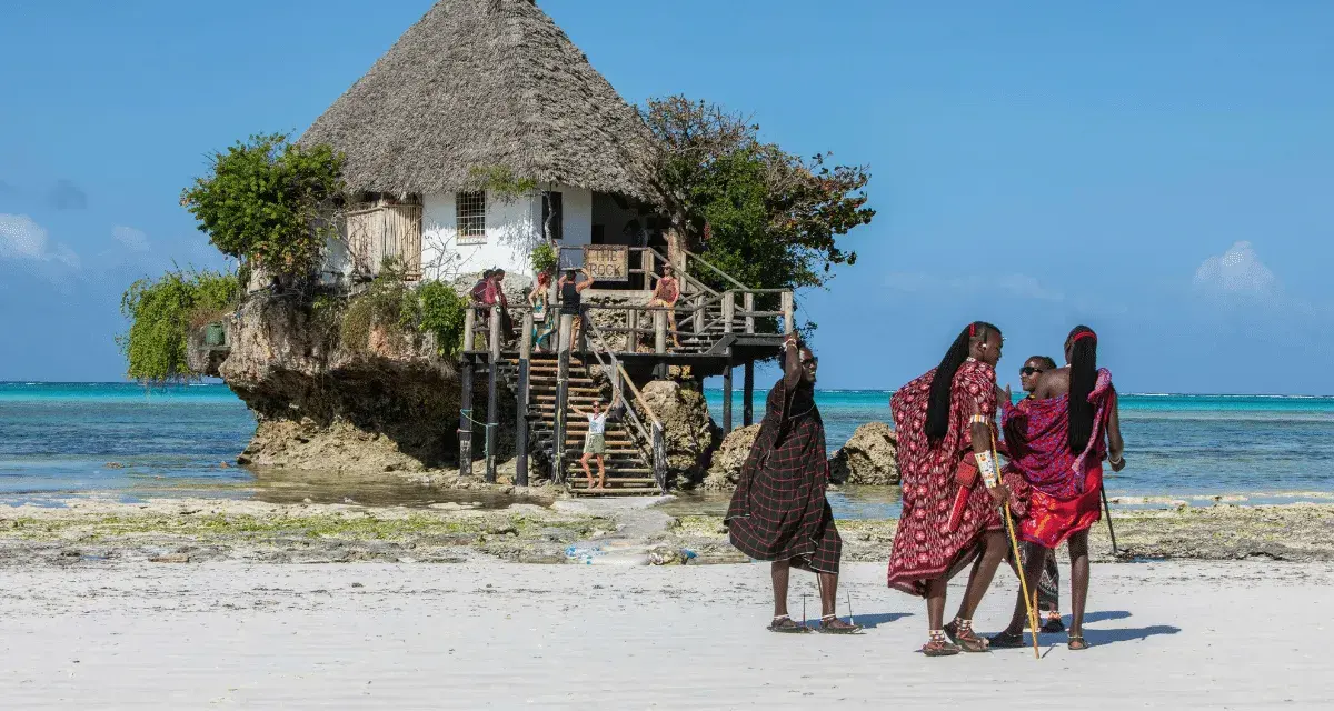 Wspaniały marzec na Zanzibarze. Ludzie w tradycyjnych strojach spacerują po plaży przy restauracji "The Rock" na skale.