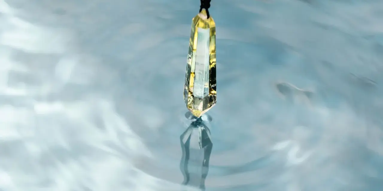 Un cristal de selenita cuelga sobre agua azul, reflejando su brillo. Quizás es porque la selenita necesita agua para purificarse.