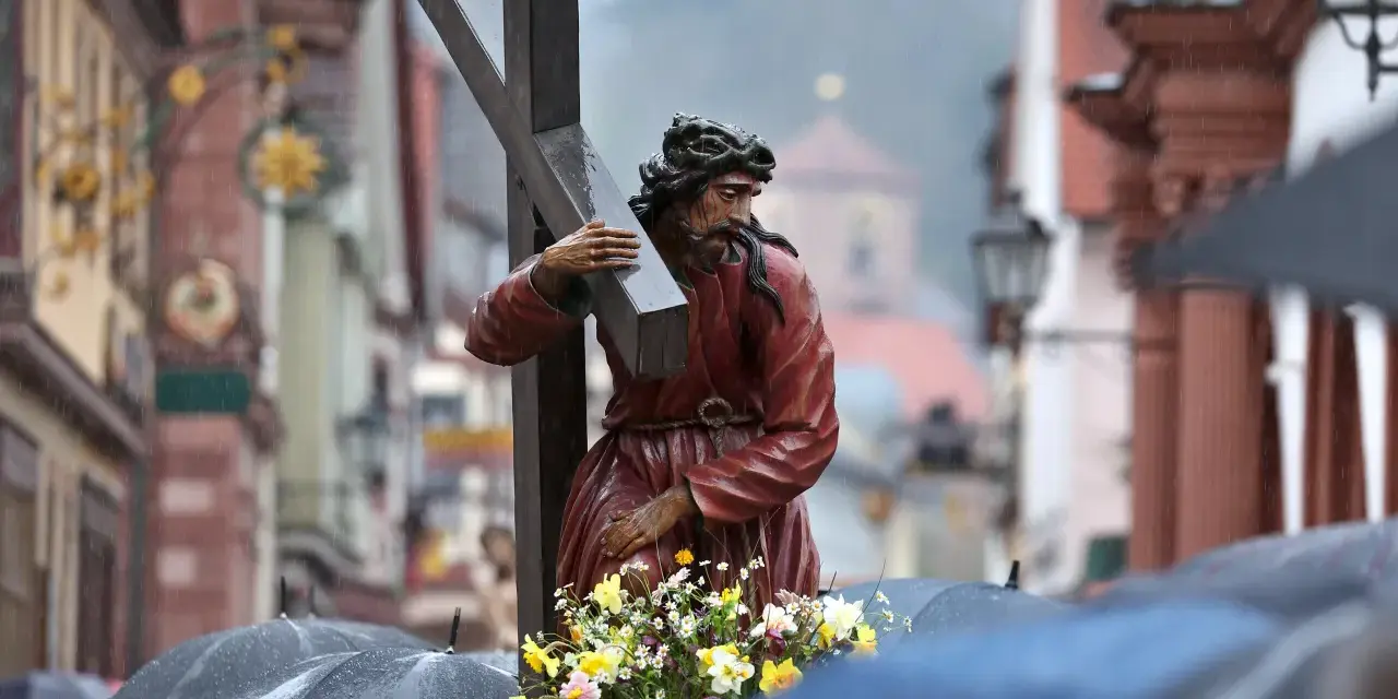 Prozession am Karfreitag: Jesus trägt das Kreuz. Gläubige mit Regenschirmen gedenken.