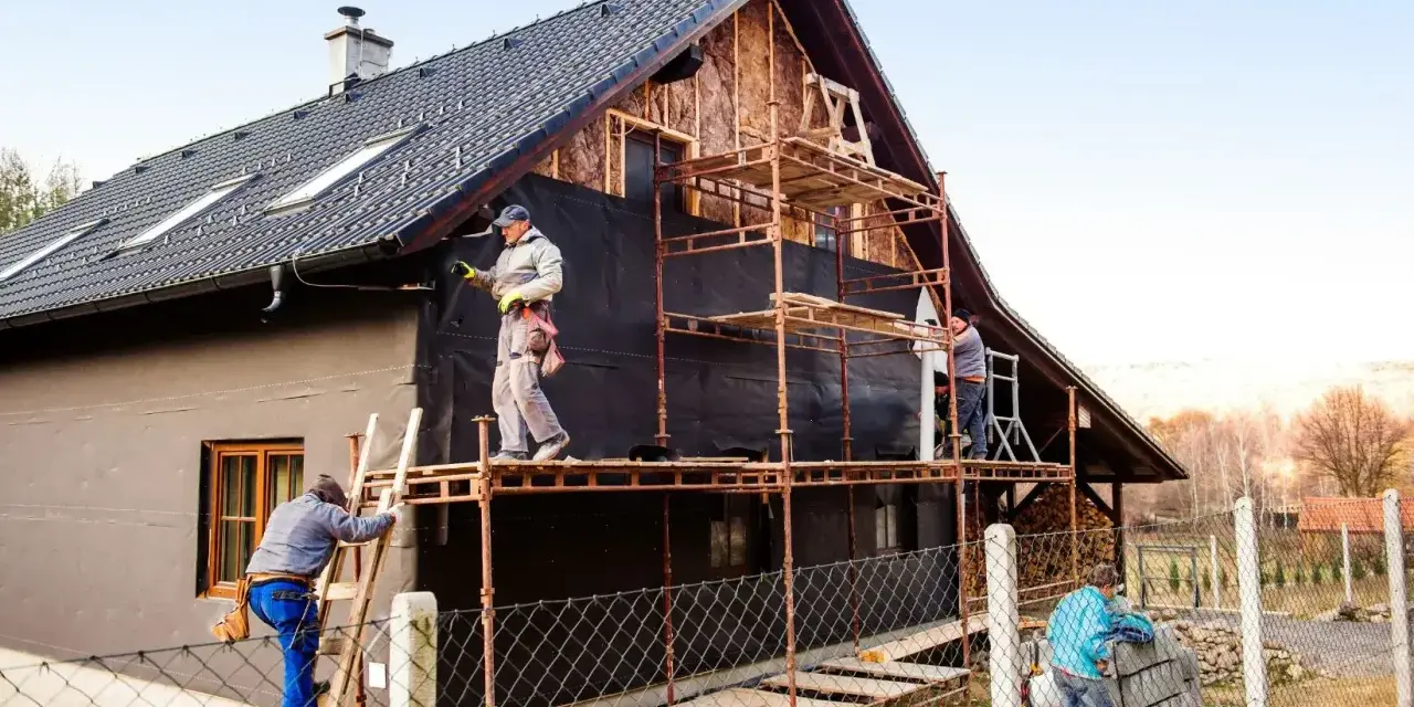 Pracownicy na rusztowaniach ocieplają dom. Określenie ceny ocieplenia za 1m2 robocizna jest kluczowe dla tego projektu.
