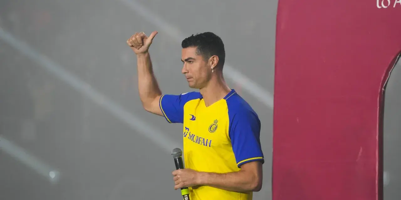 Cristiano Ronaldo w koszulce Al Nassr z mikrofonem, pokazuje kciuk w górę.