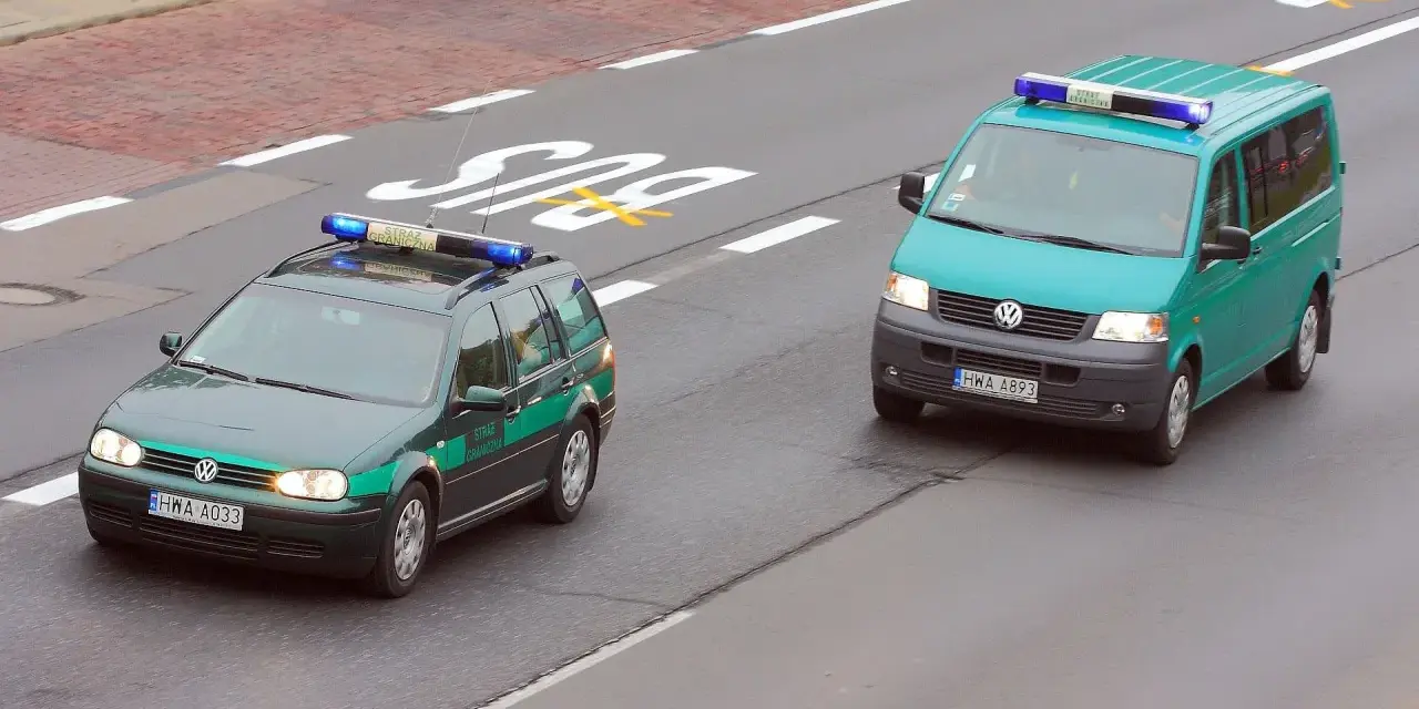 Dwa pojazdy uprzywilejowane Straży Granicznej, zielony kombi i turkusowy van, jadą drogą.