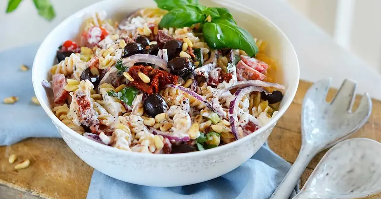 En härlig italiensk pastasallad med rotfrukter, oliver, soltorkade tomater och pinjenötter, toppad med färsk basilika.