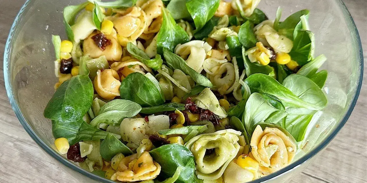 Kolorowa sałatka z tortellini, kukurydzą i suszonymi pomidorami w szklanej misce.