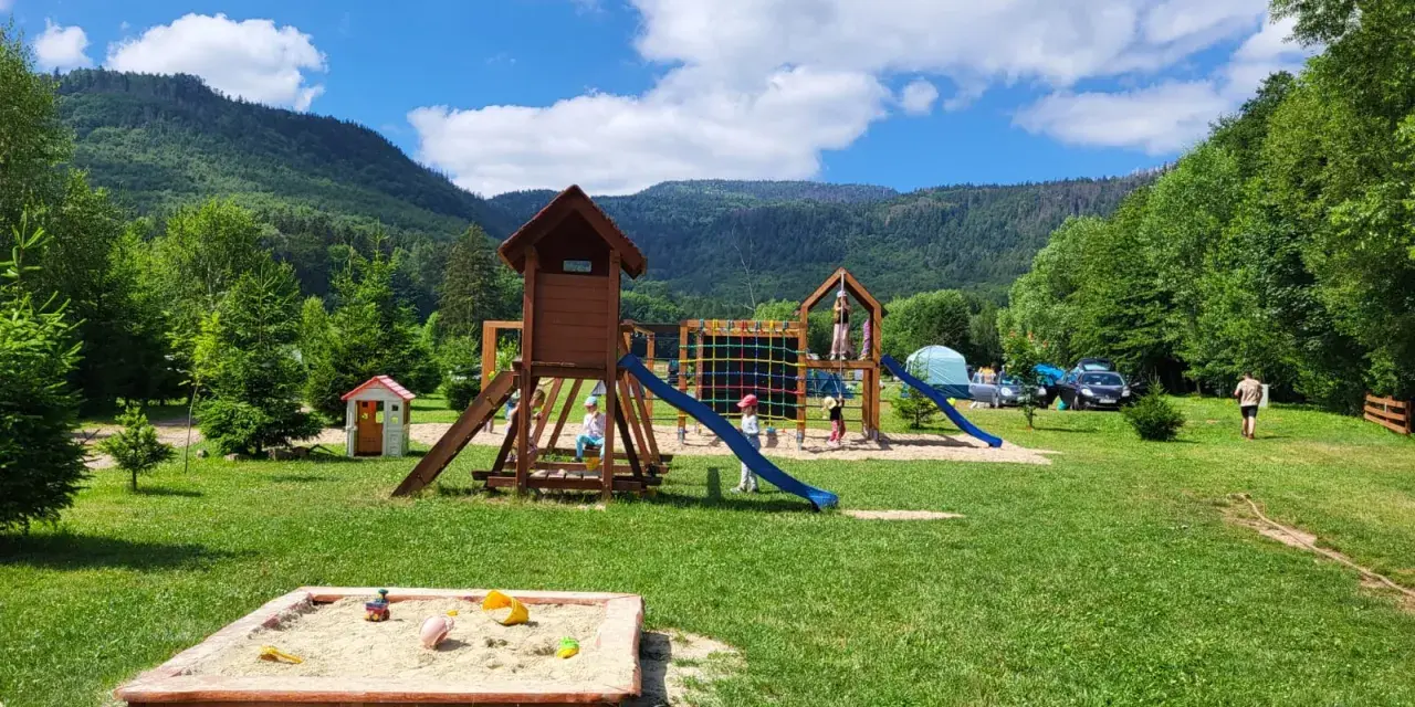 Plac zabaw dla dzieci na terenie radków camping. Piaskownica, zjeżdżalnie i drabinki w otoczeniu zieleni i gór.