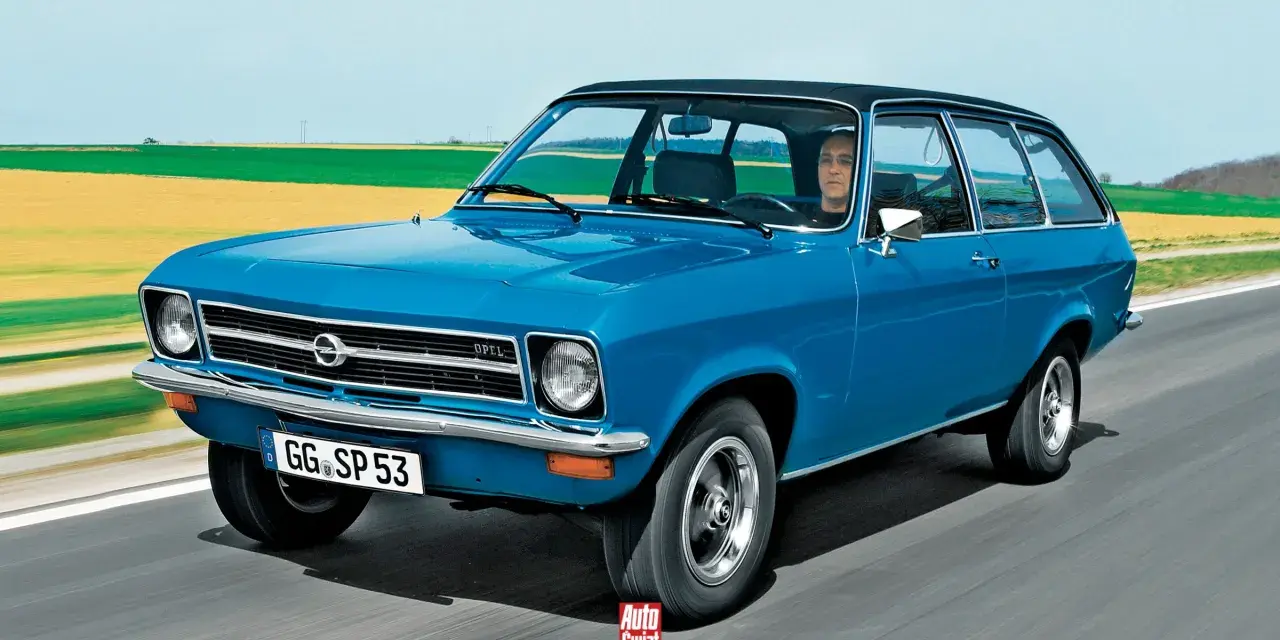 Niebieski Opel Ascona w wersji kombi jedzie po drodze, za nim pola i niebo.