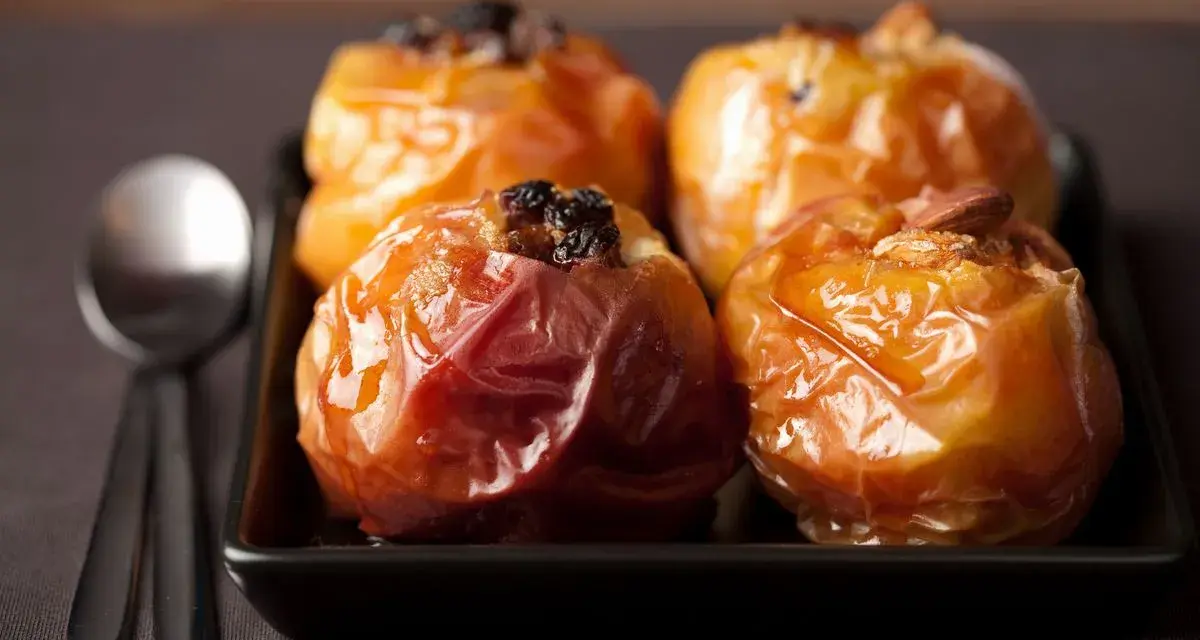 Mele cotte in friggitrice ad aria, caramellate e ripiene di uvetta e mandorle, pronte per essere gustate con un cucchiaio.