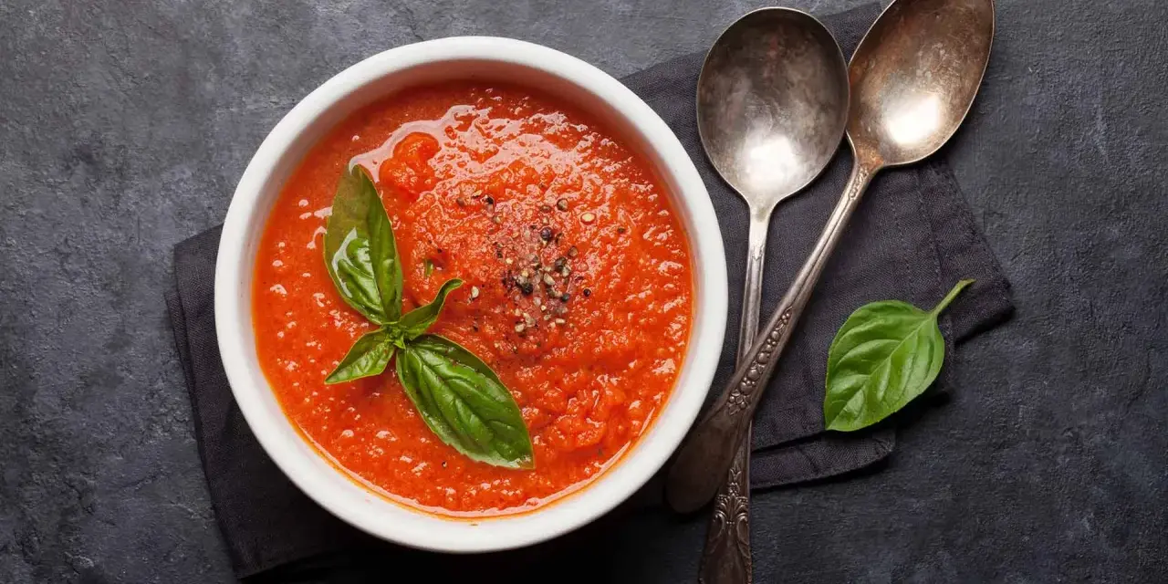 Eine Schüssel mit leckerer, italienischer Tomatensauce, garniert mit Basilikum und Pfeffer. Daneben liegen zwei Löffel.