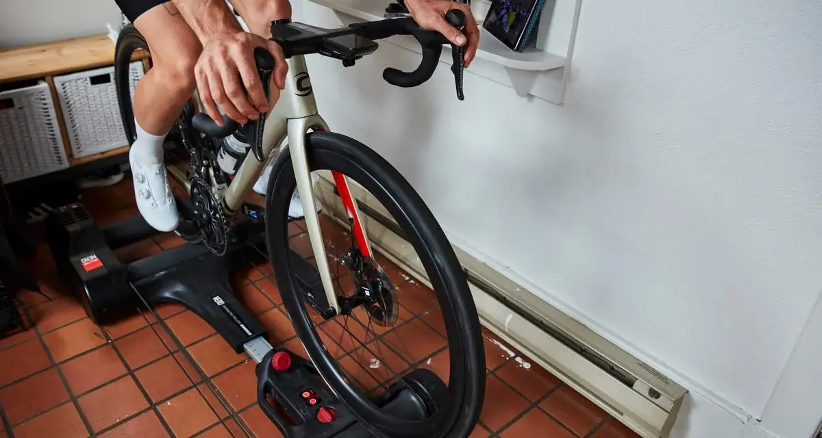 Cyclist on bike rollers, a dynamic alternative to a trainer, rides indoors while watching a tablet.
